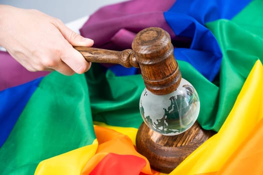 Woman judge holding a gavel on a crystal globe on a rainbow flag. LGBT community.