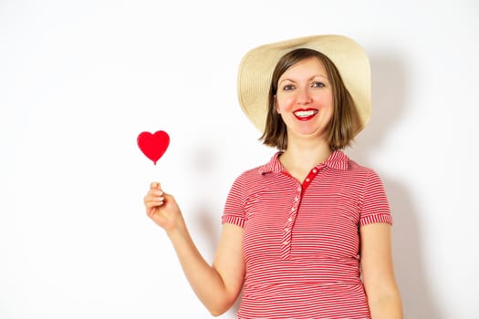 Beautiful girl in summer hat on white background with heart lollipop in her hand for Valentines Day.