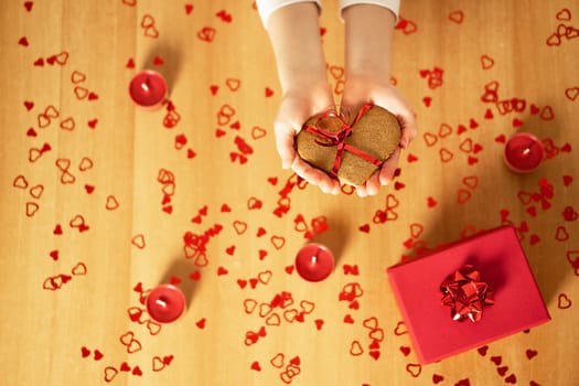Child hands holding homemade baked heart cookie on the background of the many red hearts and lights