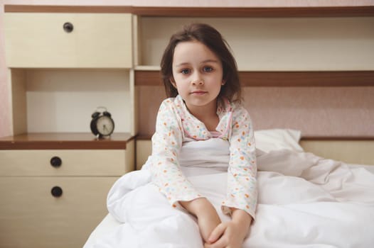 Portrait of a Caucasian beautiful child girl in pajamas, sitting in the bed at her cozy bedroom
