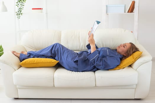 Carefree young woman in cozy pajamas resting on sofa at home - wellbeing and comfort morning concept