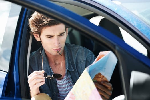 Navigating my journey. Young man sitting in his car and inspecting a map while holding his sunglasses.