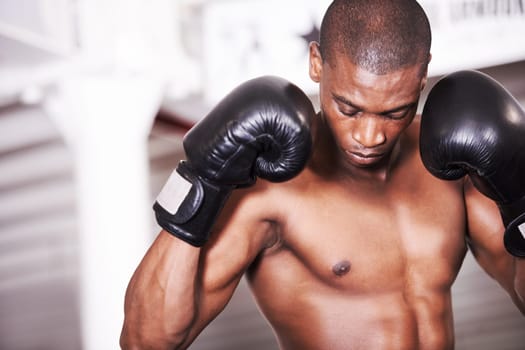 Toned and ready to fight. An african american boxer looking down with his gloves up.