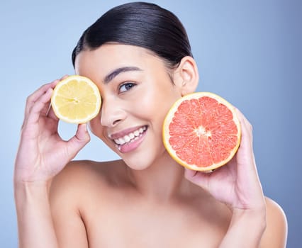 Portrait of a happy mixed race woman holding a lemon and grapefruit. Hispanic model promoting the skin benefits of citrus against a blue copyspace background