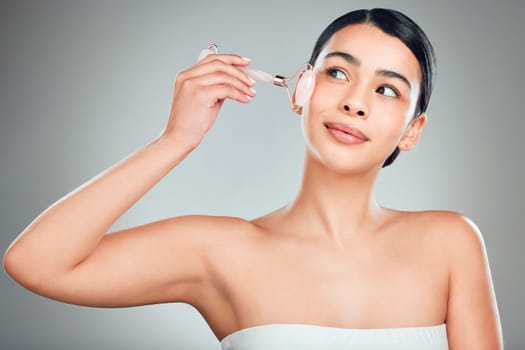 One beautiful mixed race woman using a rose quartz derma roller during a selfcare grooming routine. Young hispanic woman using anti ageing tool against grey copyspace background