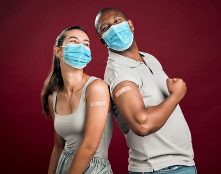 Covid vaccinated African american man and mixed race woman standing back to back. Two people wearing surgical face mask isolated against red background in studio with copyspace. Showing plaster on ar