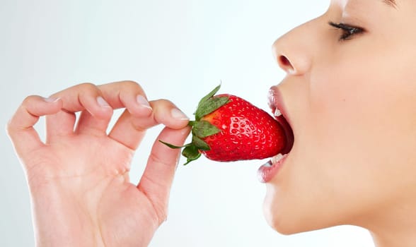 Strawberry goodness. Studio shot of an attractive young woman biting into a strawberry against a light background.