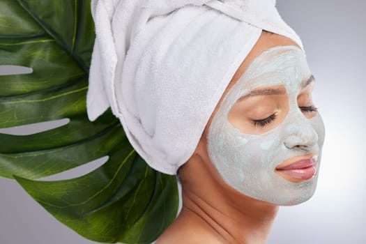 A clay mask is part of my skincare routine. an attractive young woman wearing a face mask and posing with a monstera leaf in the studio.