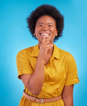 Portrait, smile and secret with a black woman in studio on a blue background standing finger on lips. Gossip, whisper and mystery withan attractive young female making a hand gesture emoji of privacy