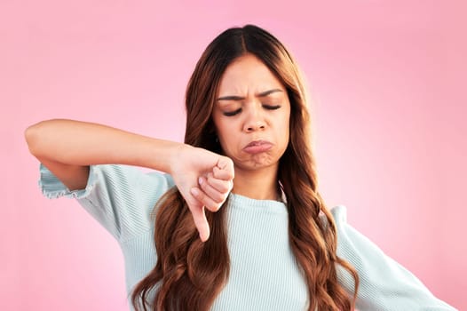 Unhappy, thumb down and sad woman in a studio with an upset, moody or disappointed face. Loser, rejection and young female model posing with a disagreement hand gesture isolated by a pink background.