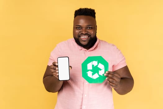 Man showing mobile phone with blank screen and recycling symbol, being happy, looking at camera.
