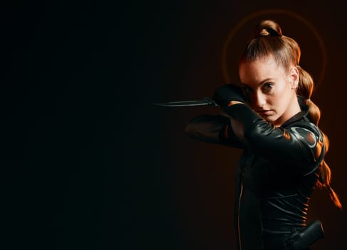 Woman, warrior and knife in studio with space for action, fight and safety from danger. Strong female model, assassin or agent in scifi leather cosplay costume with weapon on a dark mockup background