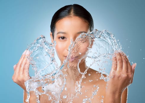 Goodbye dry skin. an attractive young woman posing against a blue background in the studio and splashing her face with water.