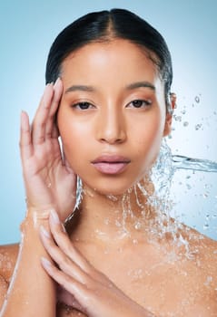 My skin needs the extra moisture today. an attractive young woman posing against a blue background in the studio while being splashed with water.