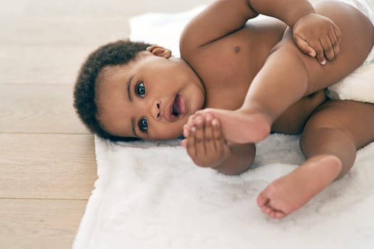 Baby, infant and black child lying down newborn relax in a home, nursery or house floor with a diaper playing with feet. Cute, adorable and innocent little kid with happiness in development