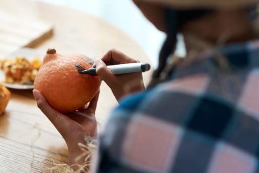 You have to start with a design. an unrecognizable person drawing on a pumpkin at home.