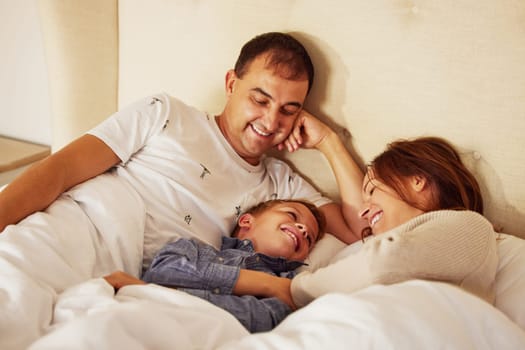 Who needs an alarm when you have children. a happy couple lying in bed and bonding with their son in the morning.
