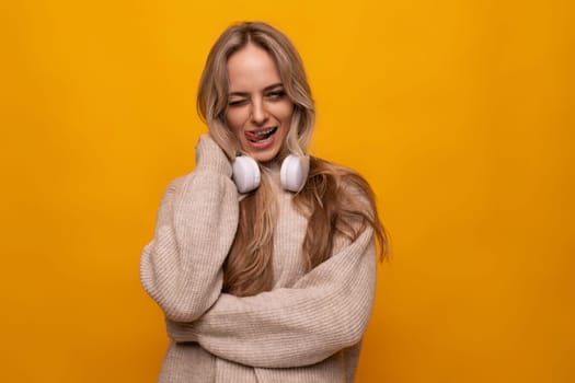 girl grimaces with big headphones in a studio with a yellow background