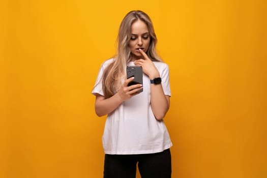 blond girl counts in her mind looking at the smartphone screen on an orange background