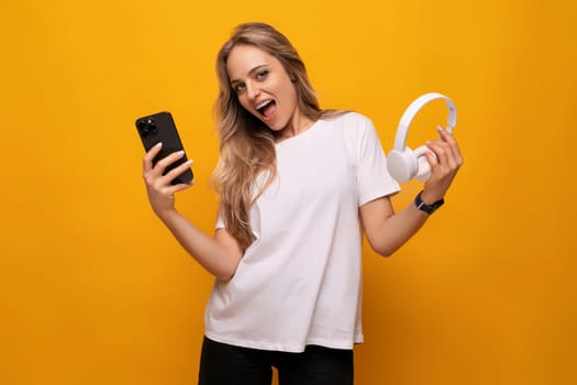 a girl with a smartphone and headphones in her hands uses an application on an orange background