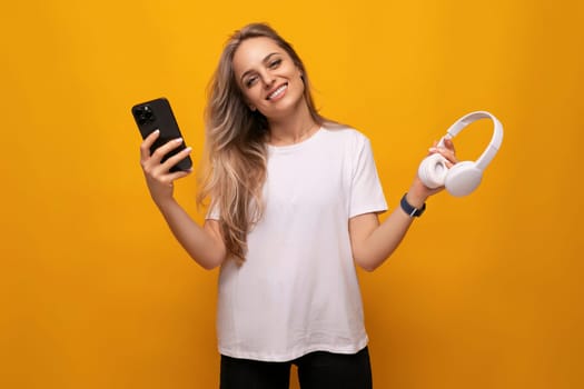girl with a smartphone and headphones in her hands on a yellow background