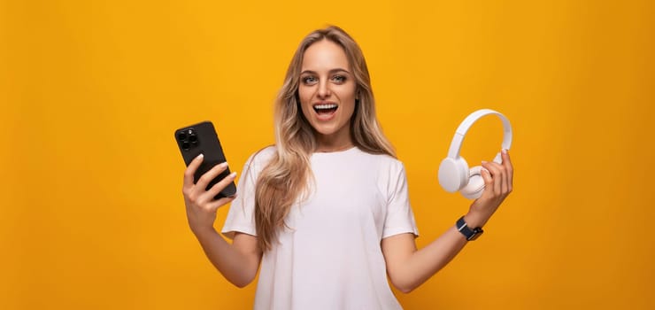girl with a smartphone and headphones in her hands on an orange background