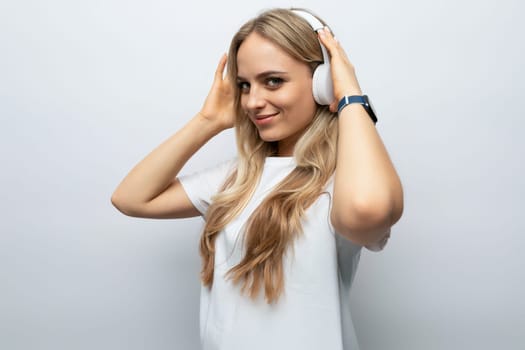 joyful young woman in white headphones listening to podcasts on white background