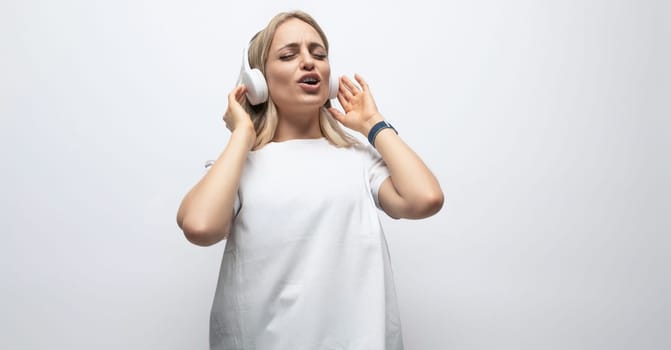 young woman having fun with music with wireless headphones in a studio with white walls