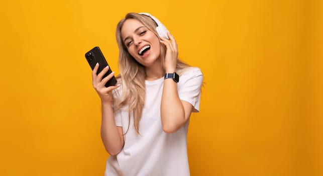 girl breaks away to music in headphones holding a phone in her hands on a studio yellow background