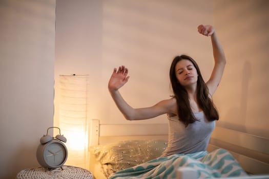 A girl with long hair on her bed stretches after sleeping.