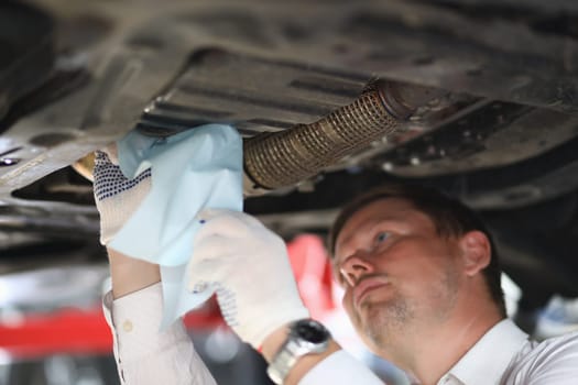 Auto mechanic inspects car leak and suspension parts of raised car with napkin at repair station