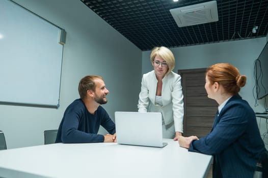 Blond, red-haired woman and bearded man in suits in the office. Business people are negotiating in the conference room.