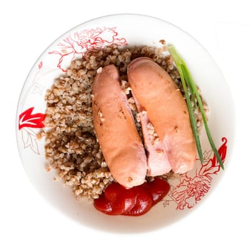 A plate of buckwheat and wieners with ketchup and a stalk of green onions on a white background