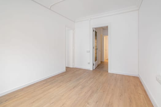 Empty white room with wooden laminate flooring and an open door in new house. Concept of preparing the premises for occupancy and carrying out cosmetic repairs. Copyspace