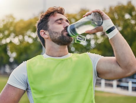 Drinking water, fitness and hydration with a sports man outdoor for a competitive game or event. Exercise, training and health with a male athlete taking a drink from a bottle during a break or rest