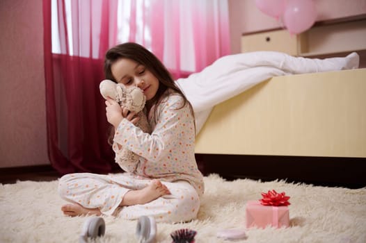 Little girl in pajamas, hugging her plush toy, sitting with her eyes closed on carpet in her bedroom before day dream