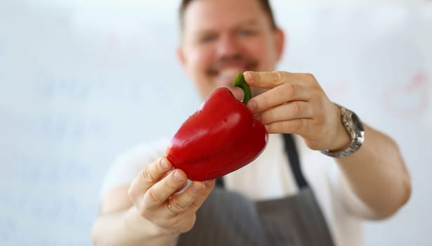 Smiling male cook holding red peppers closeup