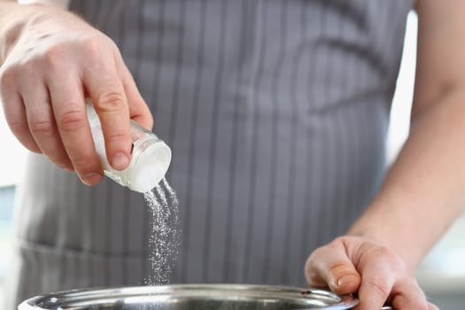 Hands of cook man salts water in saucepan in kitchen