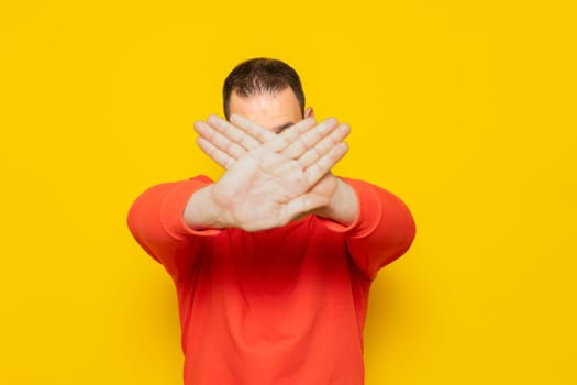 Hispanic man standing over yellow background rejection expression crossing his arms and palms covering his face making a negative sign.