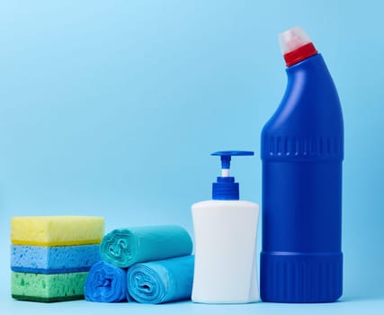 White plastic bottle with a dispenser and trash bags, sponges and a blue bottle with detergent on a blue background