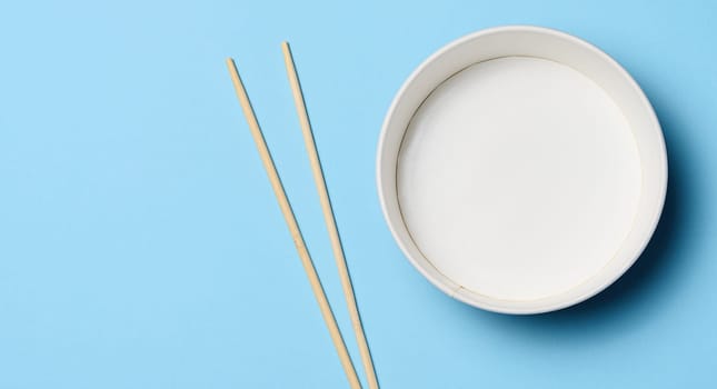 Open empty noodle bowl with and pair of wooden sticks on blue background, top view