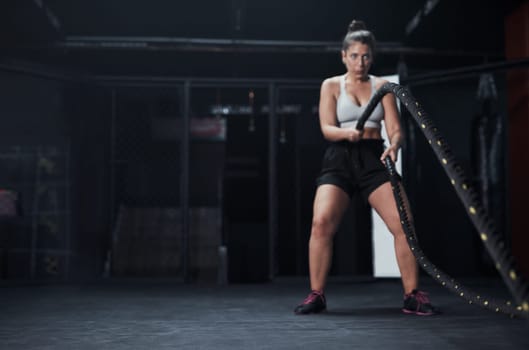 When in doubt battle it out. a young woman working out with battle ropes at a gym.