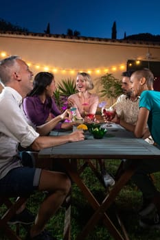 Friends enjoying cocktails after dinner outdoors in the garden. Having fun together and laughing. Vertical image. Lifestyle concept.