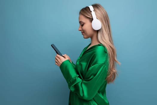 Profile photo of cute blond young adult woman listening to music with headphones on blue background