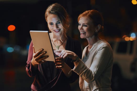 Devoted to getting the deadline done. two businesswomen using a digital tablet together outside an office at night.