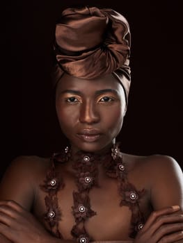 Do you know the history of the African head wrap. Studio portrait of an attractive young woman posing in traditional African attire against a black background.