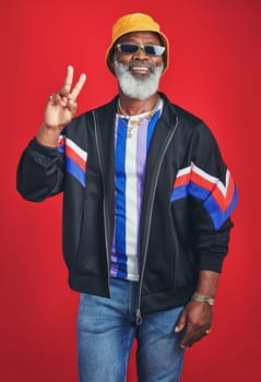 This is what you call swag. Studio shot of a senior man wearing retro attire while posing against a red background.