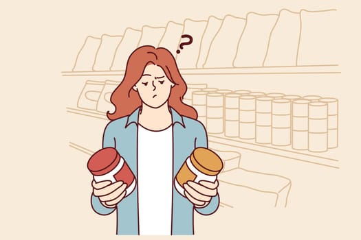 Doubting woman standing in grocery store with two similar cans and reading composition before buying