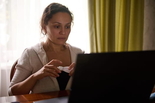 Female entrepreneur sitting at laptop and holding medicated eye drops to relieve digital eye strain. Ophthalmic concept