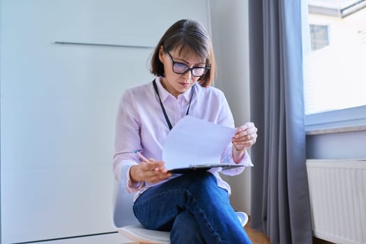 Portrait of female psychologist with clipboard sitting on chair in office